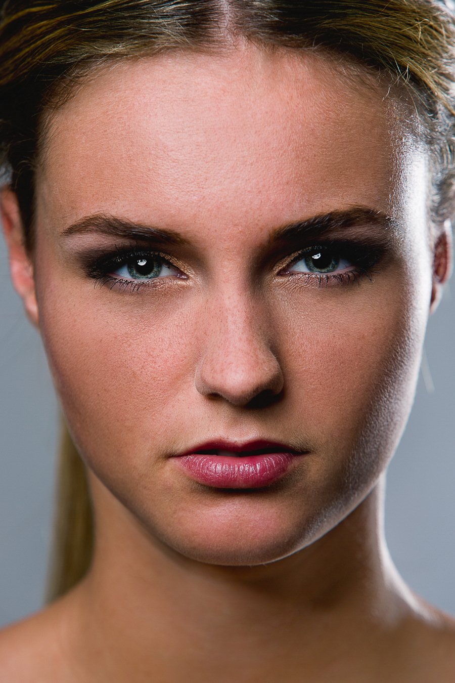 Close-up van een jonge vrouw met blauwe ogen en make-up, recht in de camera kijkend.