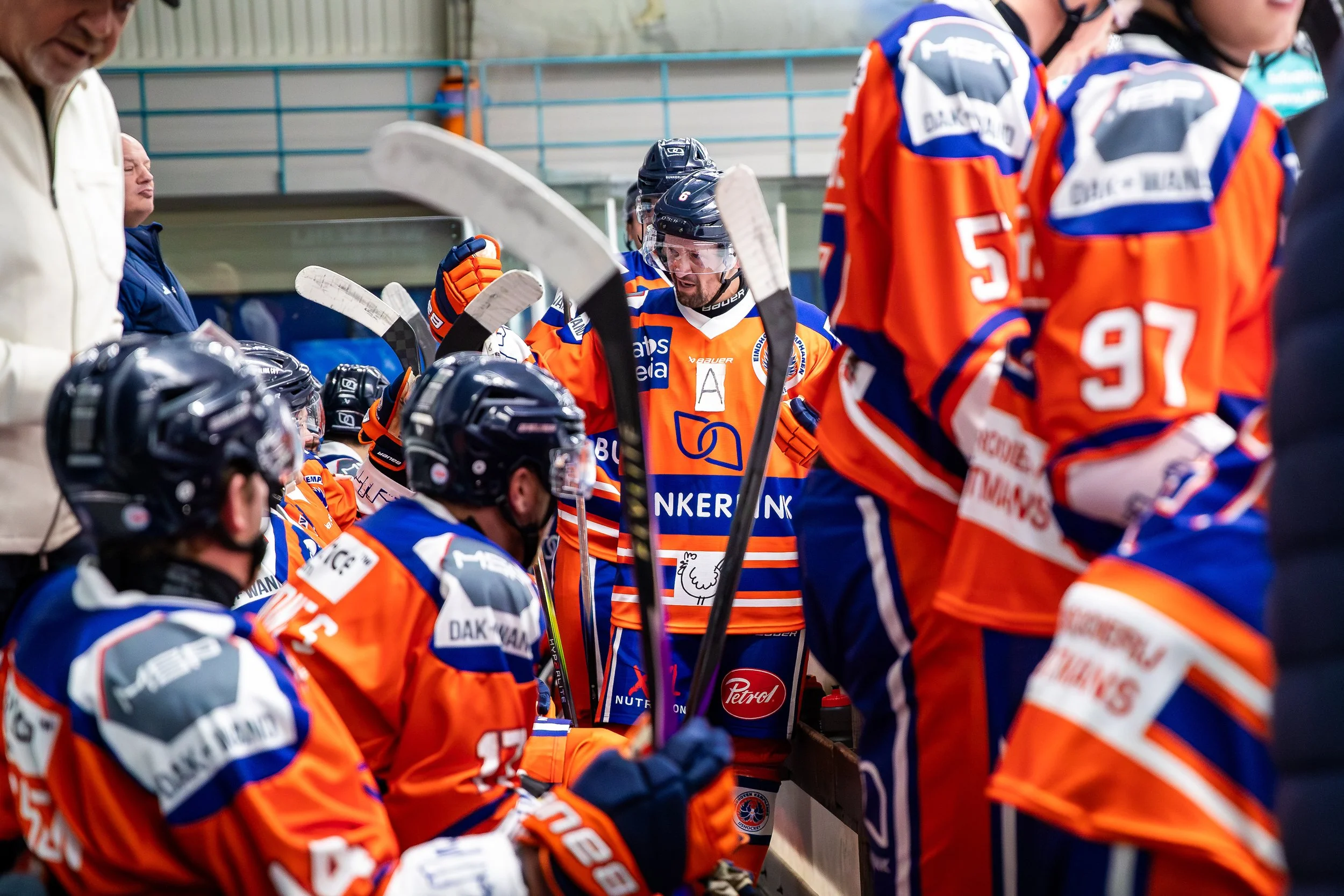 Hockeyteam in oranje en blauw uniforms tijdens een time-out op de bank.