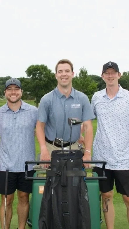 Three men standing on a golf course, smiling, with golf clubs and a golf cart.