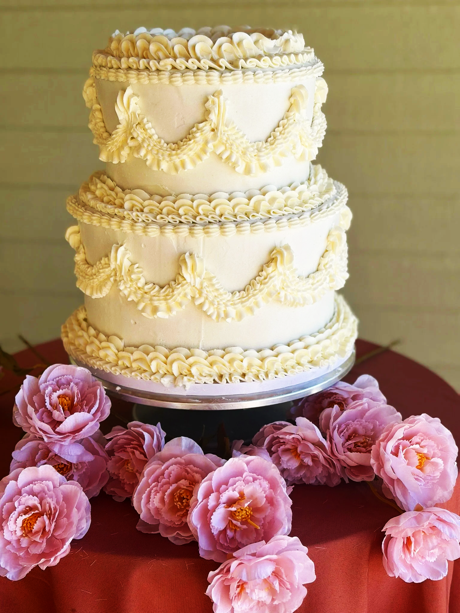 White frosted cake topped with pink chrysanthemums and green leaves, set on a silver tray with a gold cake knife and server on a white cloth napkin next to it.