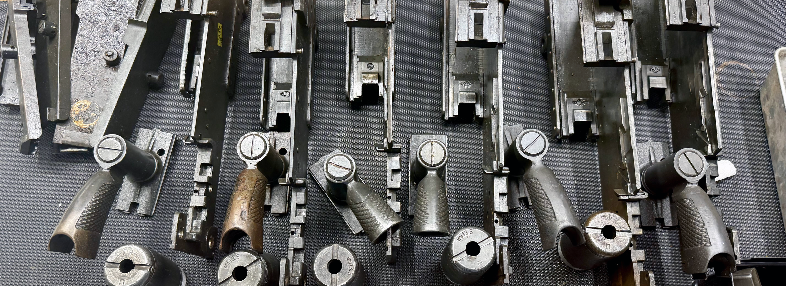 Multiple firearm frames and slides laid out on a textured surface, some showing signs of wear and rust.