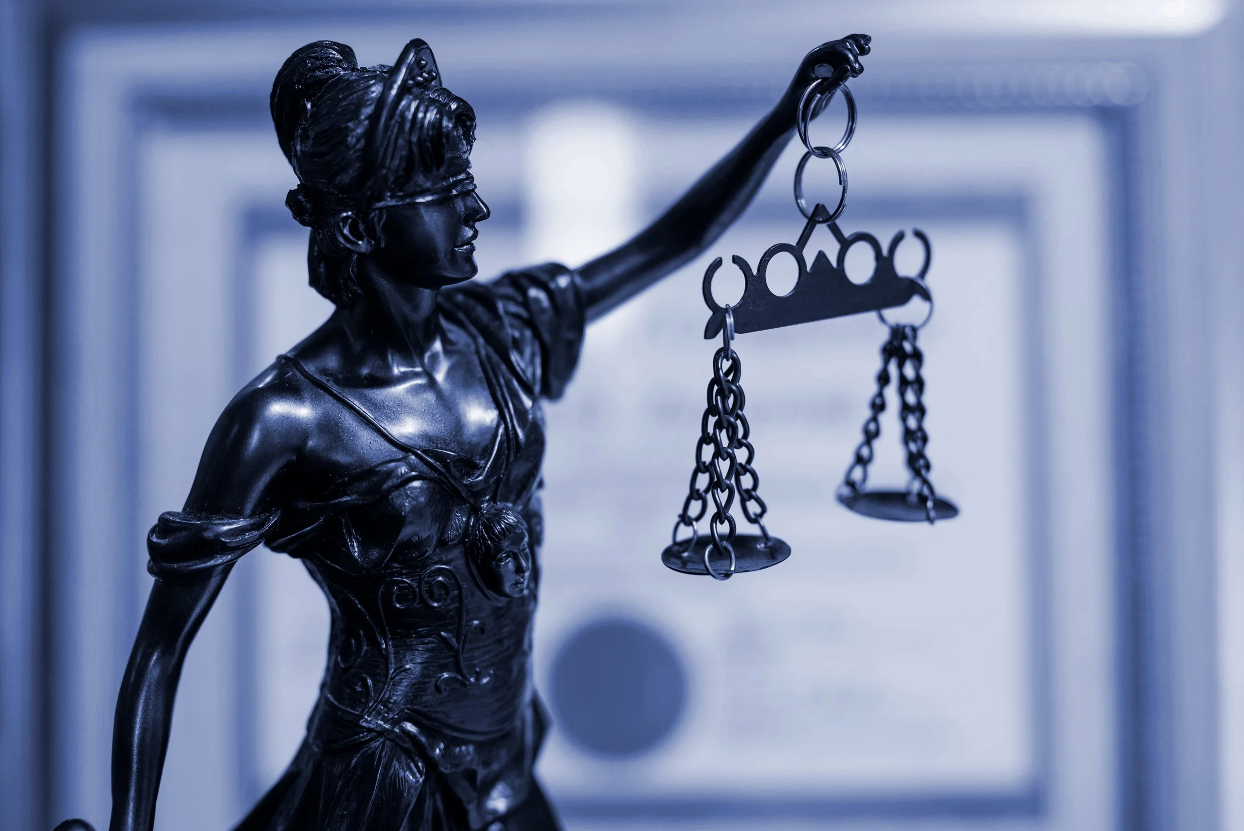 Escultura de la justicia con venda en los ojos y balanza en mano, en color oscuro.