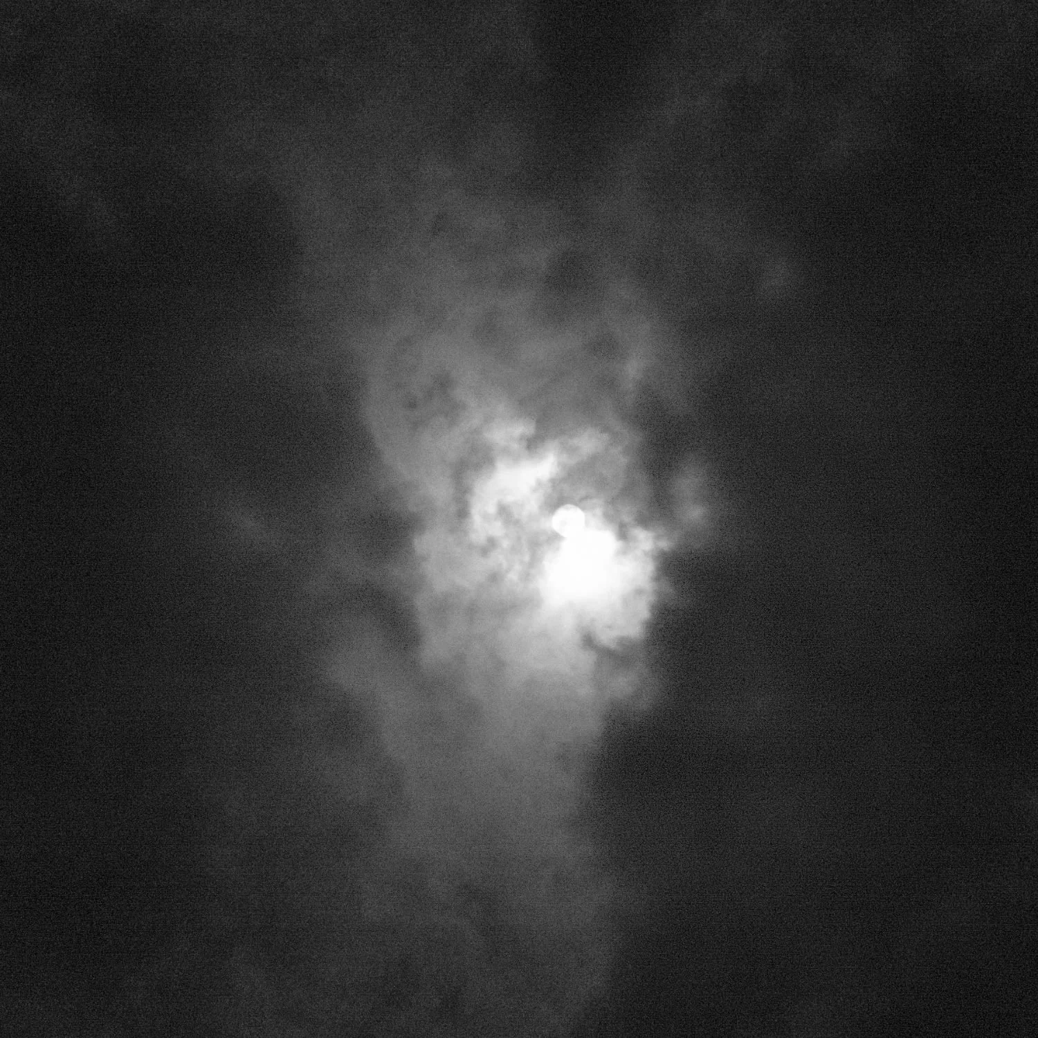 Black and white photo of the moon behind moving clouds, creating a soft and mysterious atmosphere