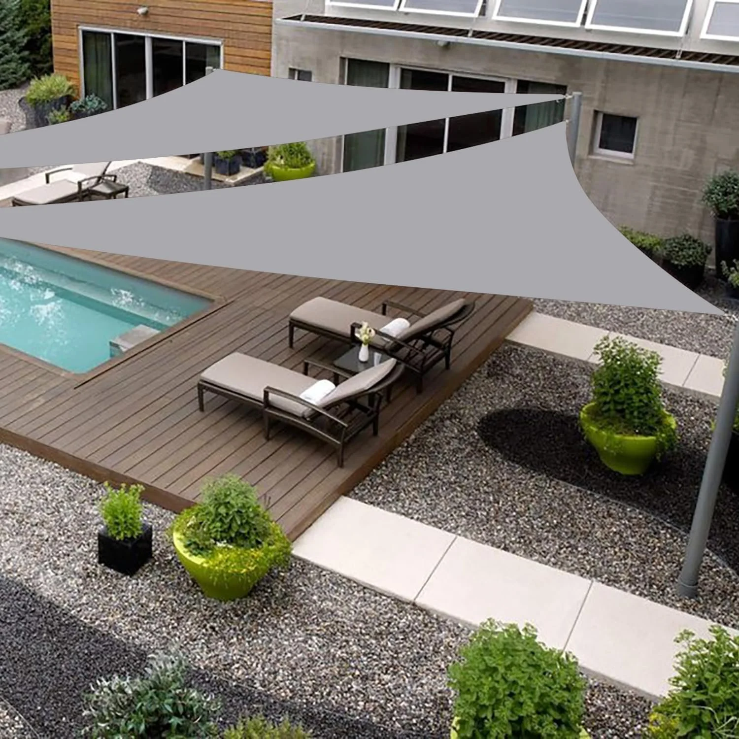 A rooftop patio with pool, wooden deck, lounge chairs, potted plants, and shade sails in an urban residential area.