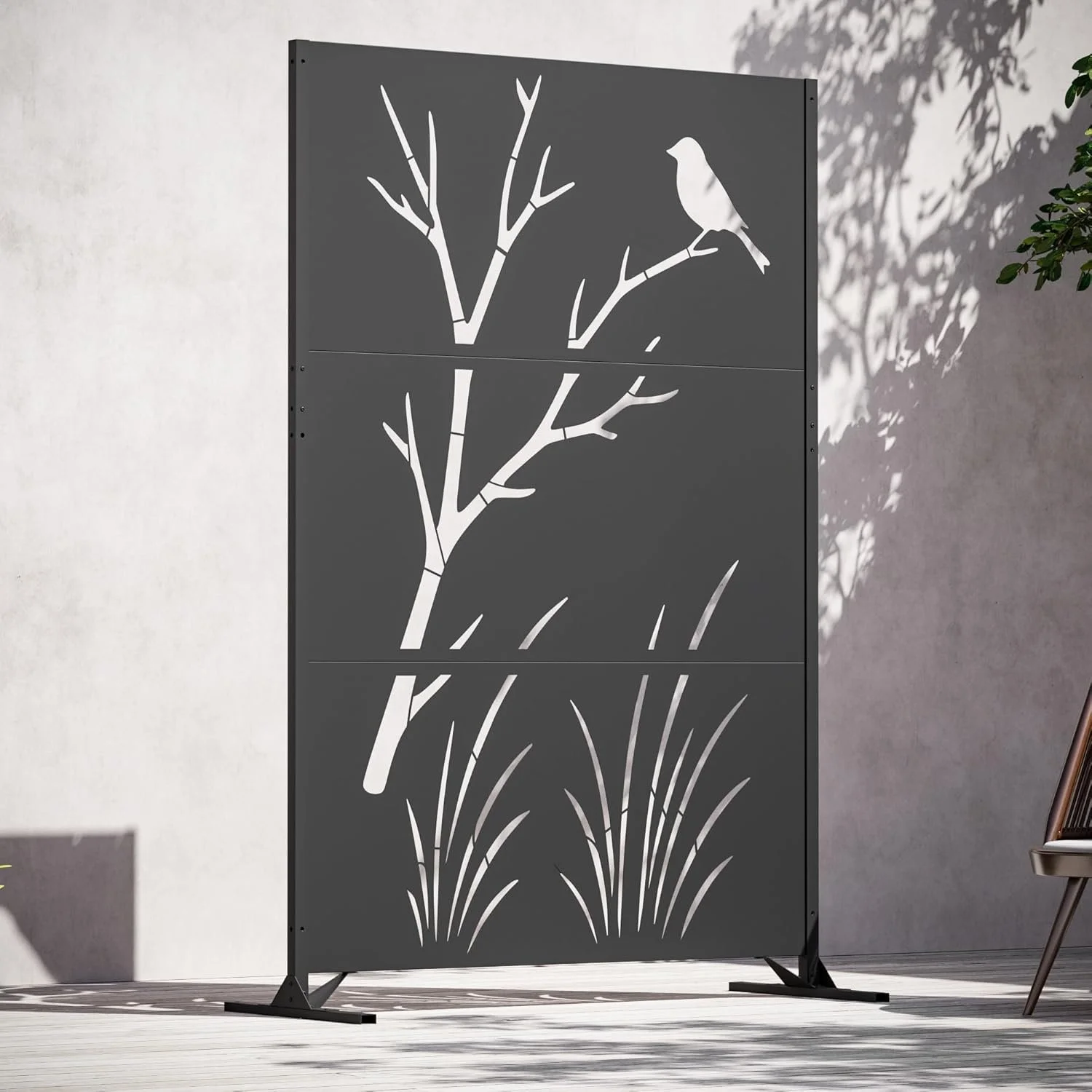 Decorative black room divider with white silhouette of a tree, a bird on a branch, and grass at the bottom, positioned outdoors on a wooden deck.