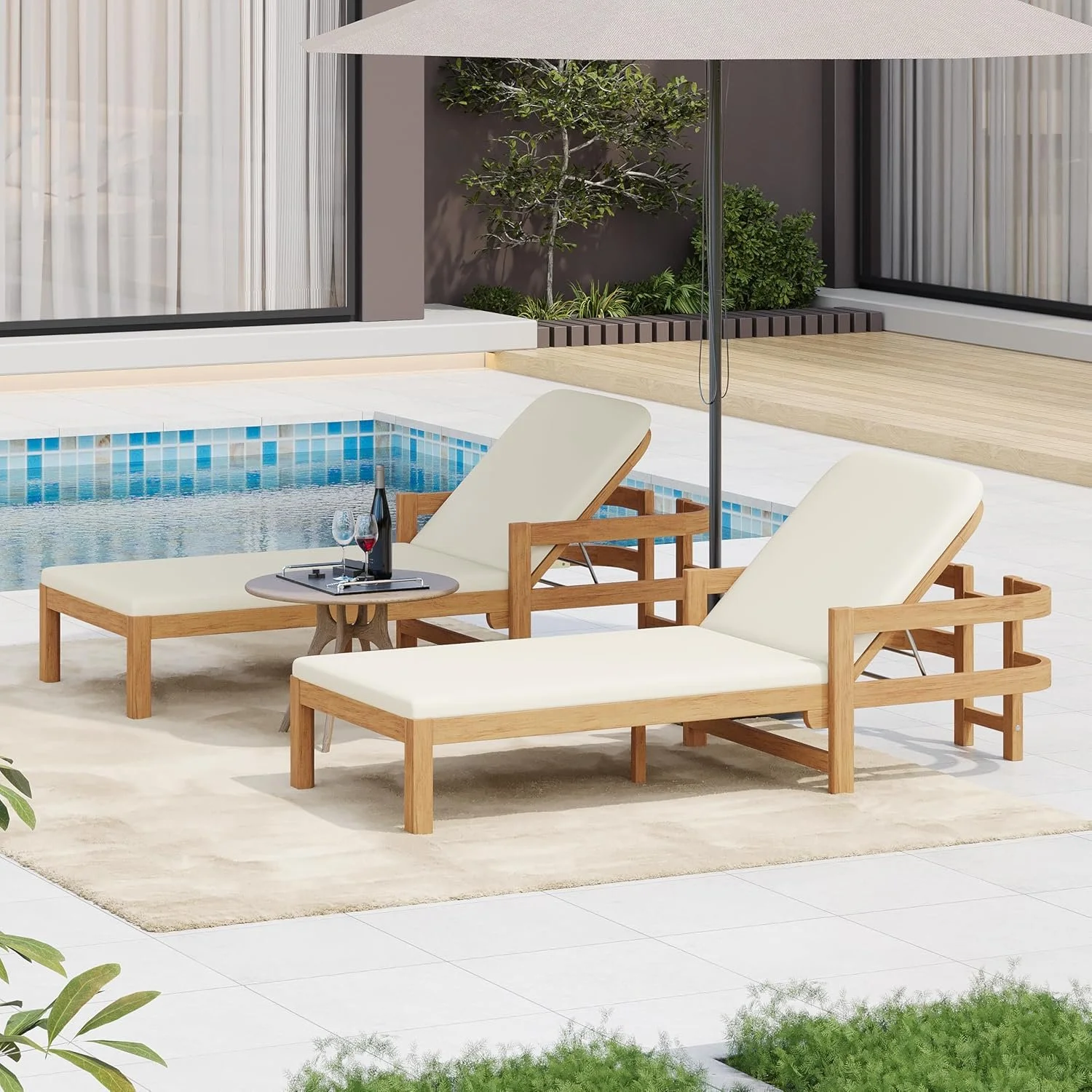 Outdoor poolside area with two white lounge chairs, a small table with a wine bottle and glasses,-benched table and a large umbrella, surrounded by a surface with tiles, plants, and a modern building with floor-to-ceiling windows in the background.