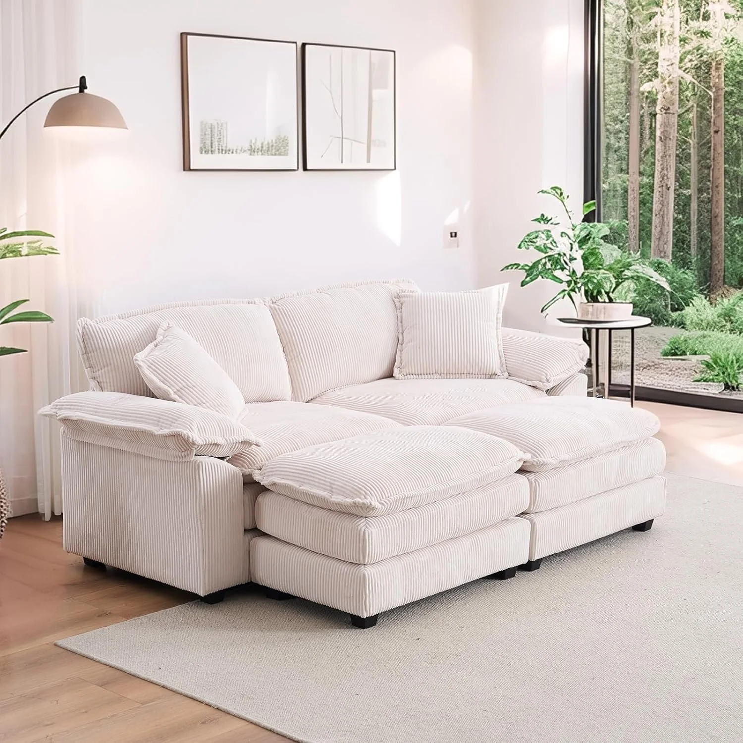 Bright living room with white striped sofa, potted plant on a side table, and large window showing a view of trees outside.