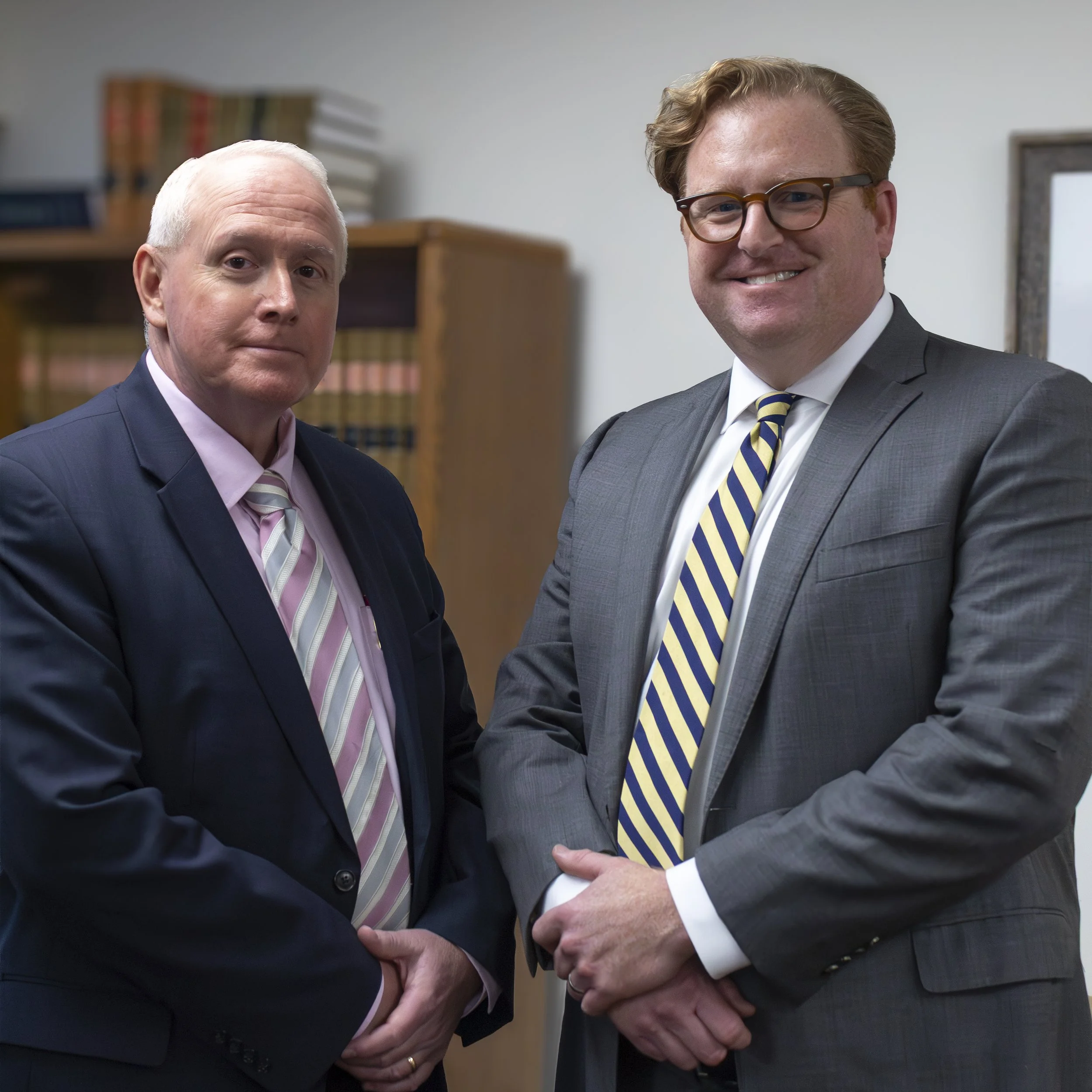 Two men in business suits shaking hands in an office, with bookshelves in the background.