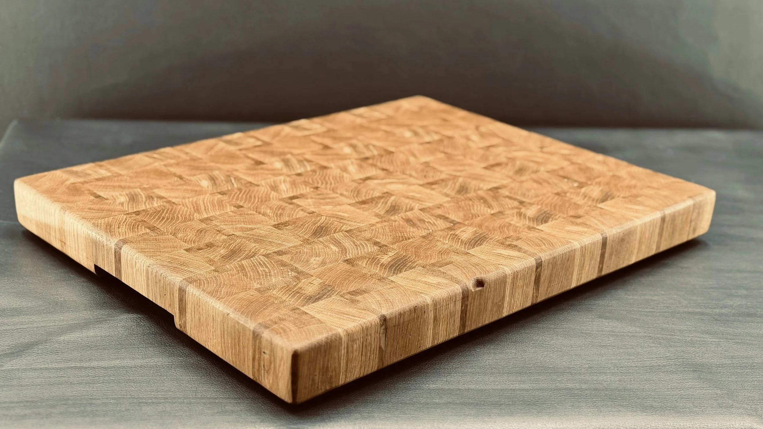 A wooden cutting board with a checkered pattern, placed on a dark surface with a gray background.
