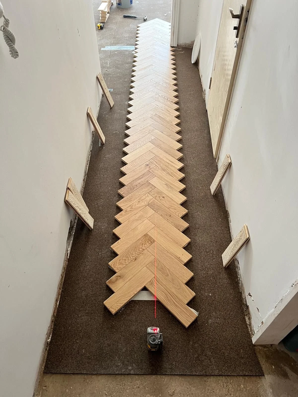 Line of wooden floorboards being installed in a narrow indoor space in Ewell, Surrey