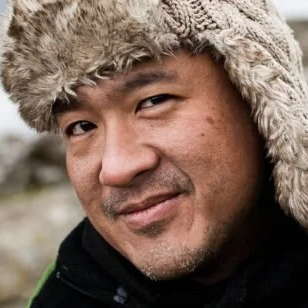 Dr Pao. Close-up of a man wearing a furry winter hat, smiling slightly outdoors.
