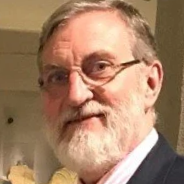 Dr Batten. A close-up portrait of an older man with gray hair, glasses, and a beard, wearing a suit jacket and a collared shirt.