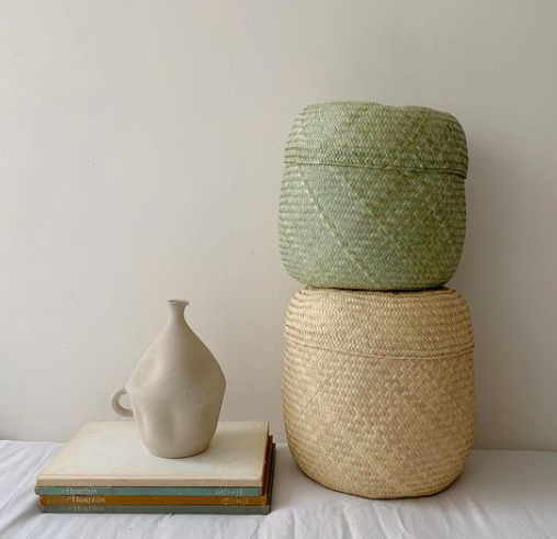 Decorative objects including a ceramic vase, two stacked woven baskets, and books on a white surface against a light-colored wall.