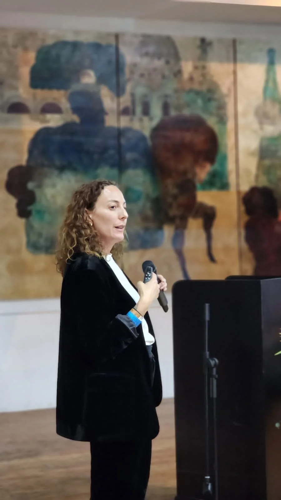 Sabrina Iken wearing a black blazer and white blouse speaking into a microphone during New World Crafts in Guatemala.