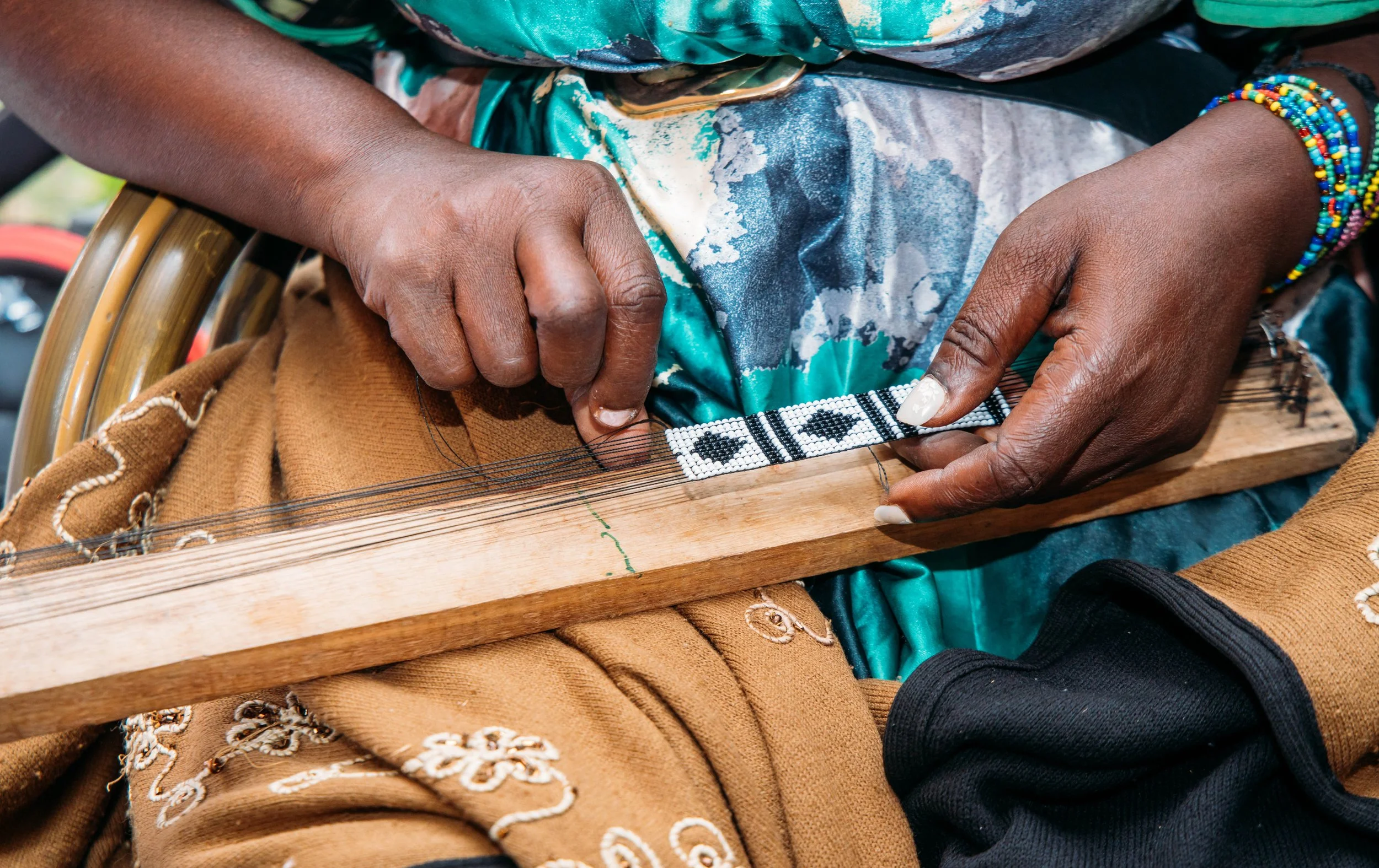 A person weaving on a wooden loom, focusing on their hands working with black and white beads in Kenya.