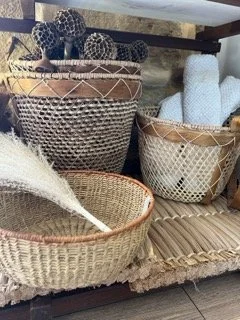A collection of woven baskets and decorative spheres on a wooden shelf, with some white rolled fabric or towels in the background.