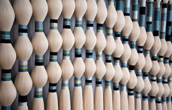 Close-up of a decorative wall made of numerous light-colored thread dowels with black and gold rings.