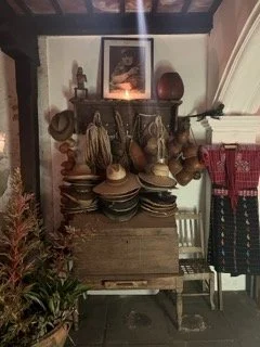 Vintage wooden cabinet with pottery and decorative items, candle, framed picture, and potted plant nearby in Antigua, Guatemala.