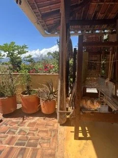 A weaving loom on a terrace with potted plants, brick flooring, and wooden structure under a blue sky in Barichara, Colombia.