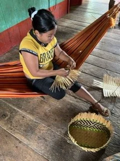 A girl weaving a hammock on a wooden porch in the Amazon, Colombia.