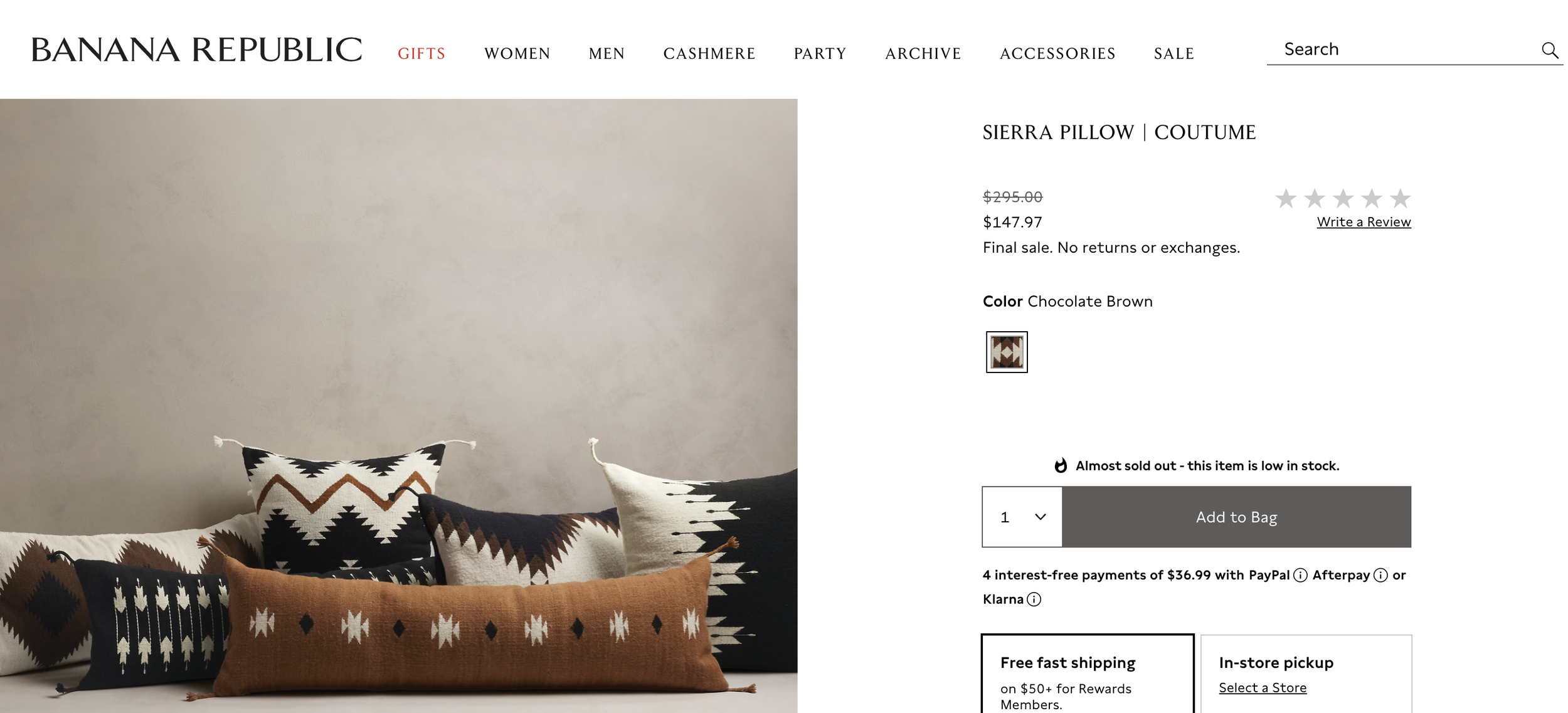 Multiple decorative pillows with southwestern patterns in black, white, and brown tones on a white surface, against a plain gray wall. Sourced by Sabrina Iken for Banana Republic, made by Coutume in Mexico.