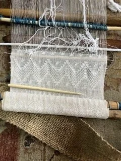 Close-up of a weaving loom with partially woven beige fabric with zigzag pattern, wooden and metal parts, and loose threads from Guatemala.
