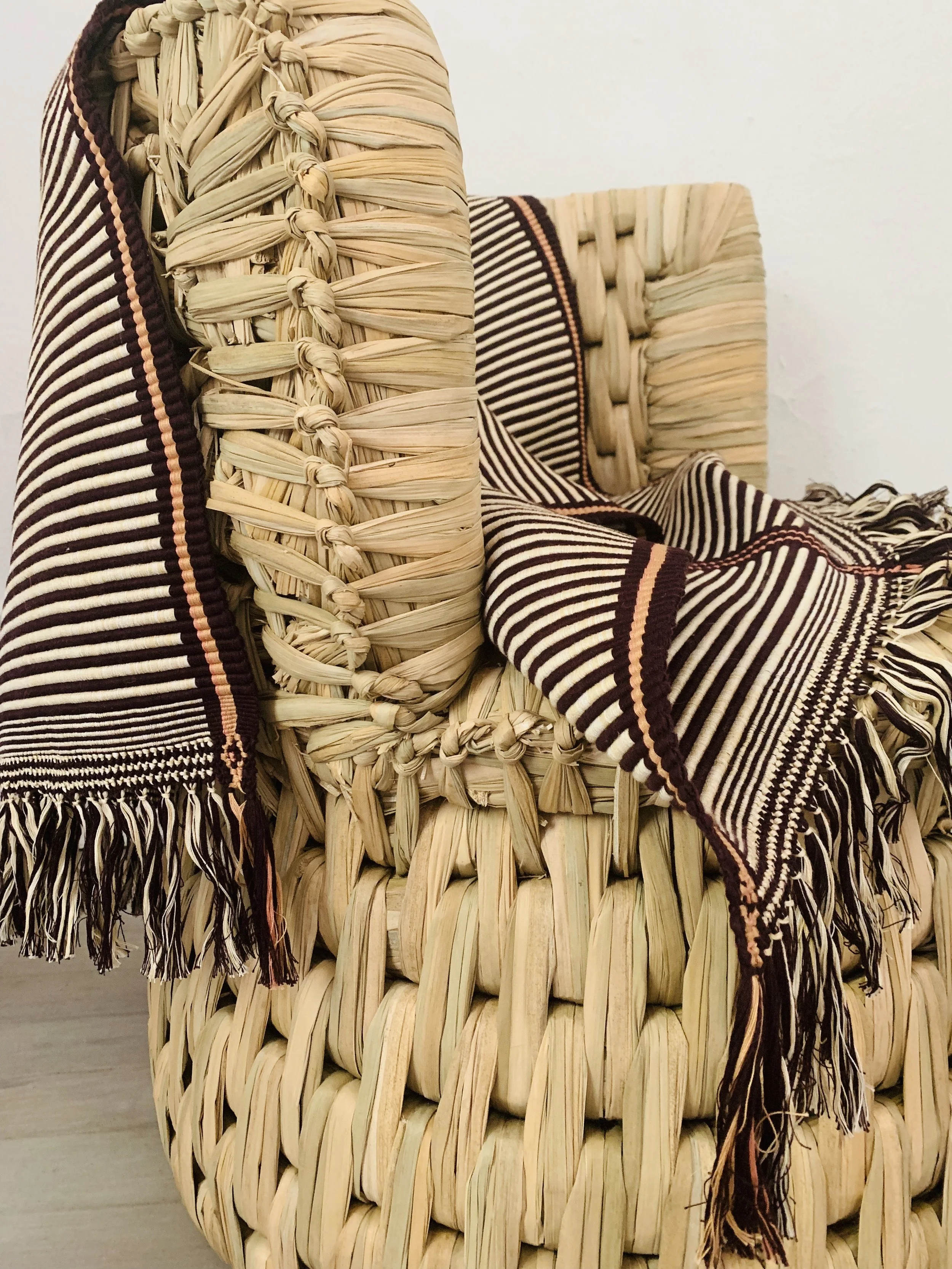 Woven chair with a striped, fringed blanket draped over it made by Atelier Iken.