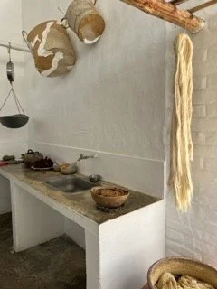 Rustic kitchen with hanging woven baskets and a bundle of threads hanging on the wall.