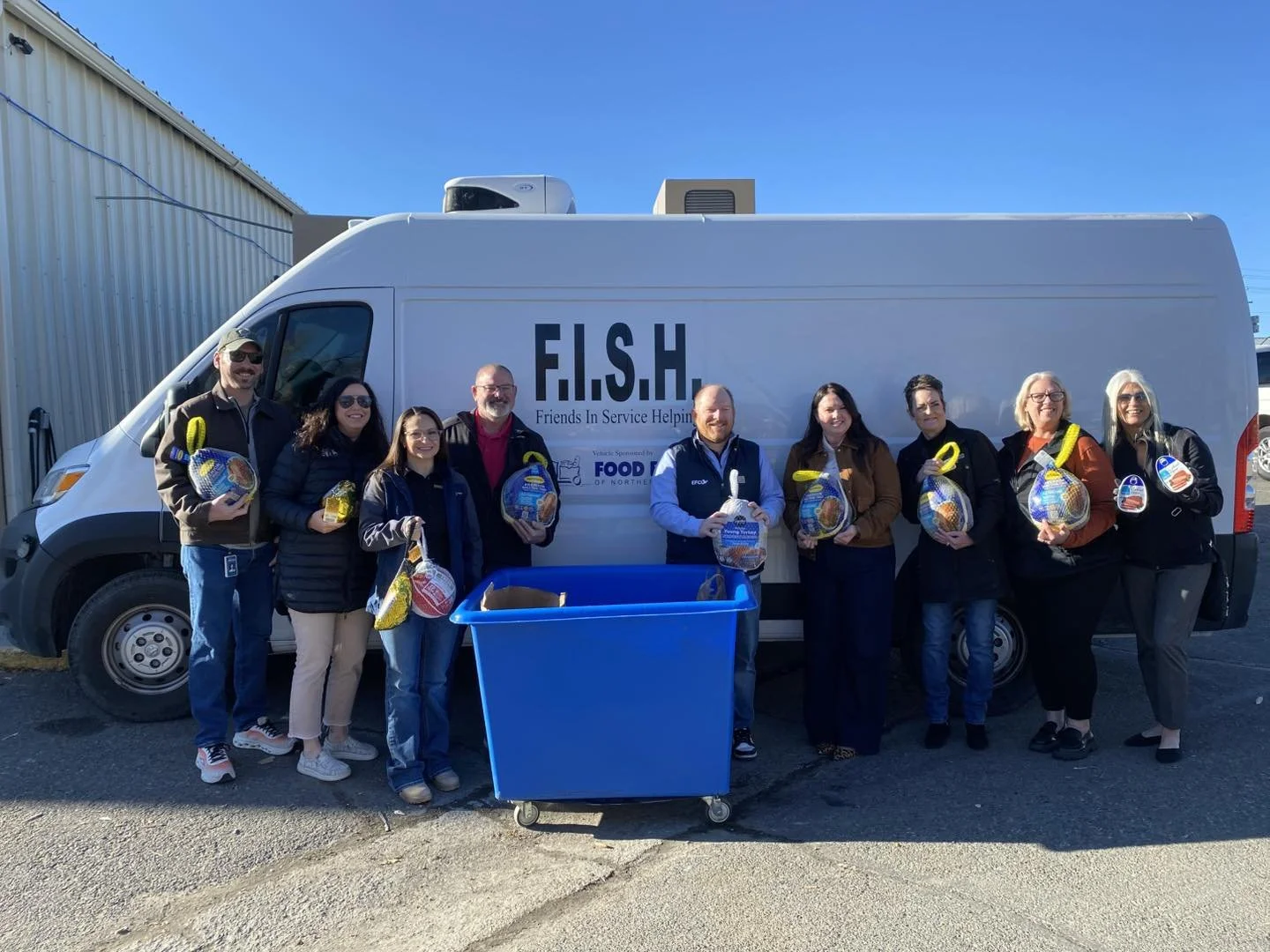 Community members pose in front of a F.I.S.H. delivery van holding donated food items.