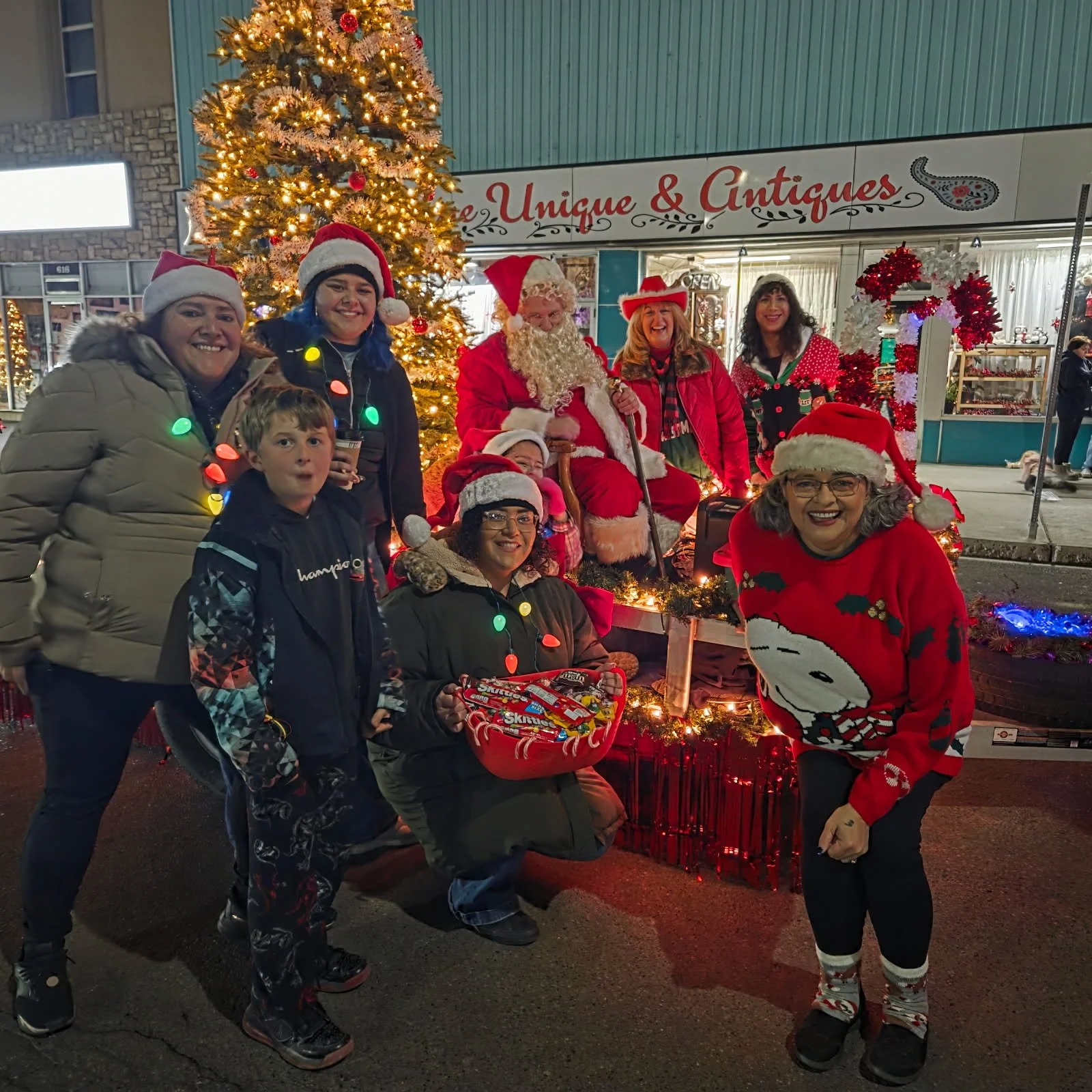 Volunteers and community members pose with Santa on a decorated holiday parade float lit with Christmas lights.