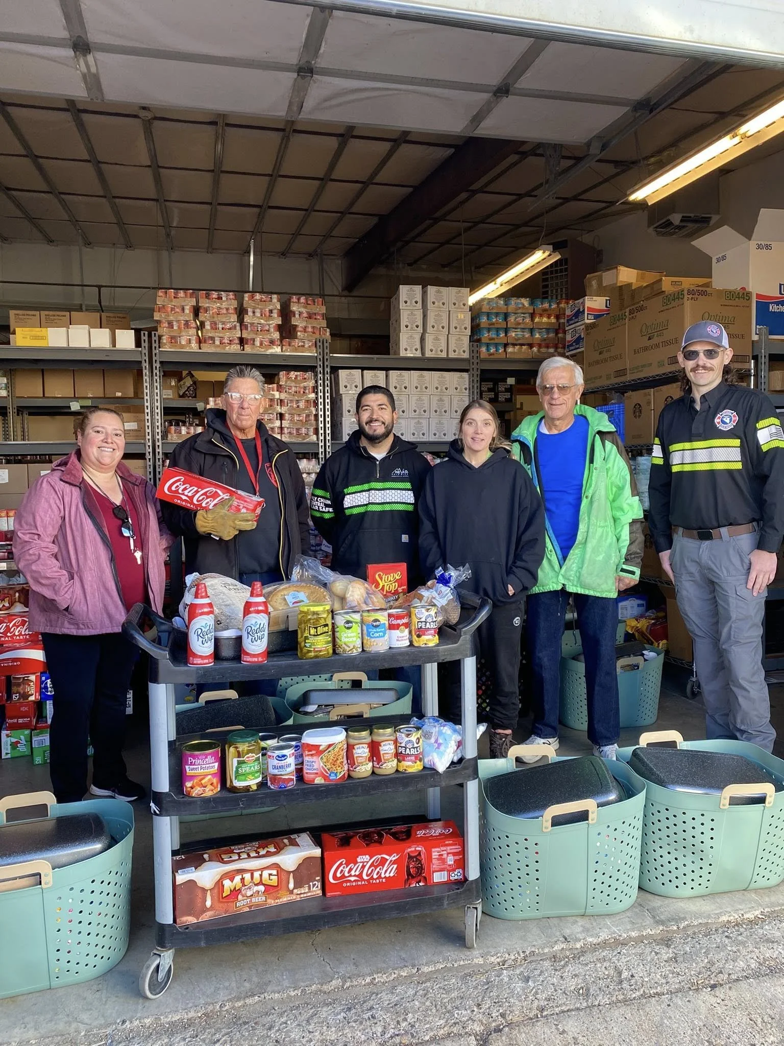 Volunteers and staff stand behind carts filled with food inside the F.I.S.H. food pantry warehouse.