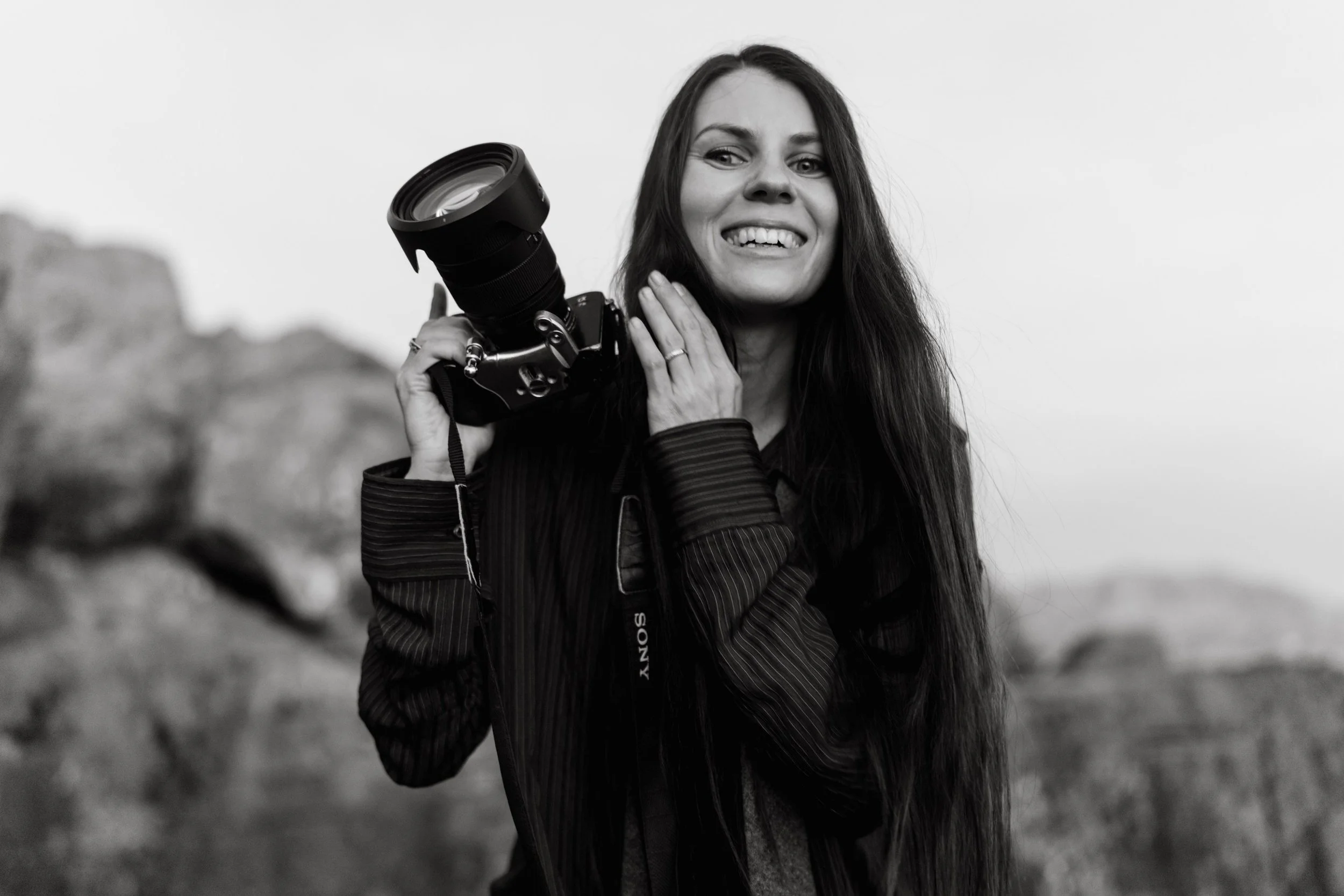 A smiling woman with long hair holding a camera.