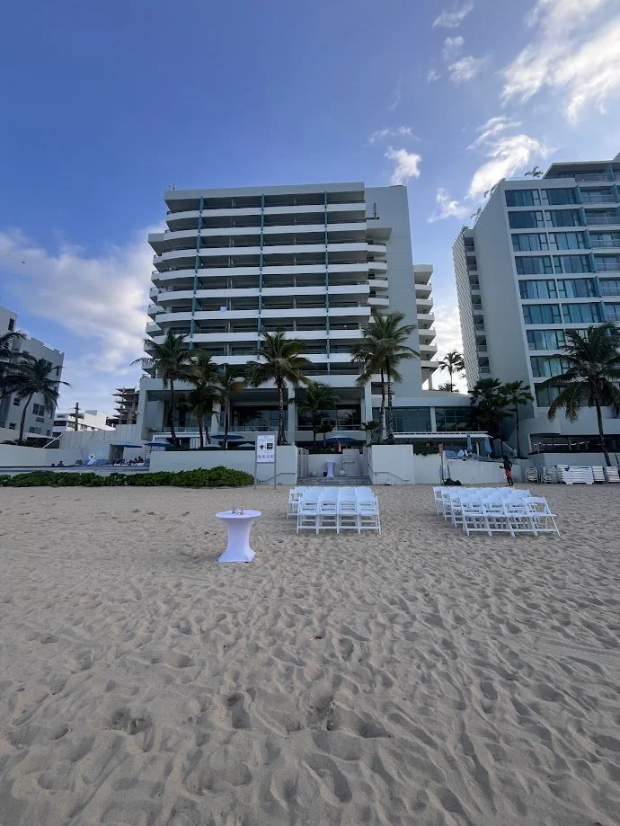 Paradise Vows PR founder Kendra smiling on the beach with a destination wedding set up in the foreground and palm trees lining the beach behind it. 