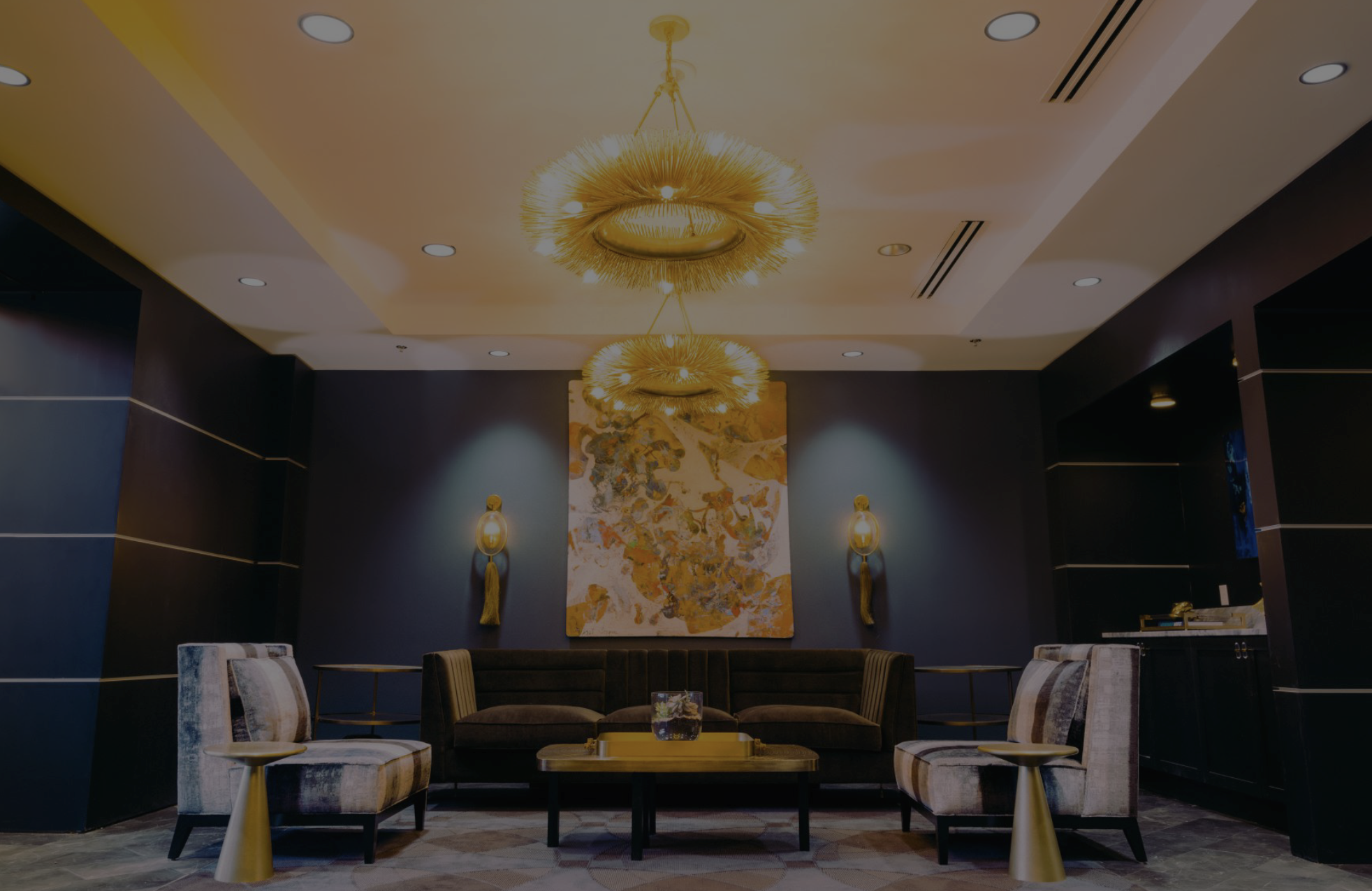 Parkhurst NuVision Clinic. Interior design. Architecture. A luxurious lobby with a dark blue wall, two wall sconces, a large abstract painting, two striped armchairs, a black sofa, a coffee table, and decorative gold lighting fixtures on the ceiling.