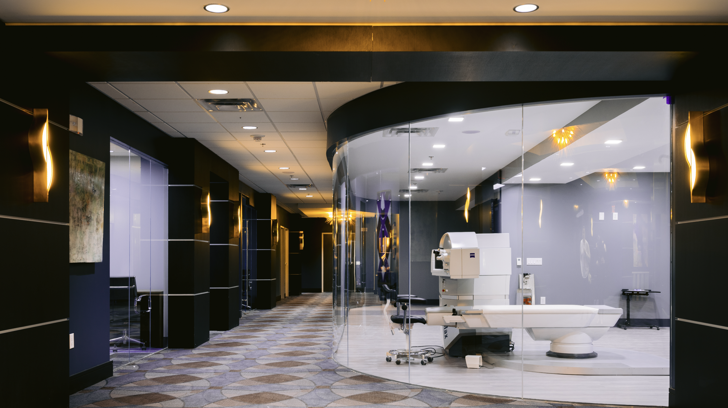 Empty medical imaging room with a large MRI machine, chairs, and a glass wall, in a modern hospital corridor.