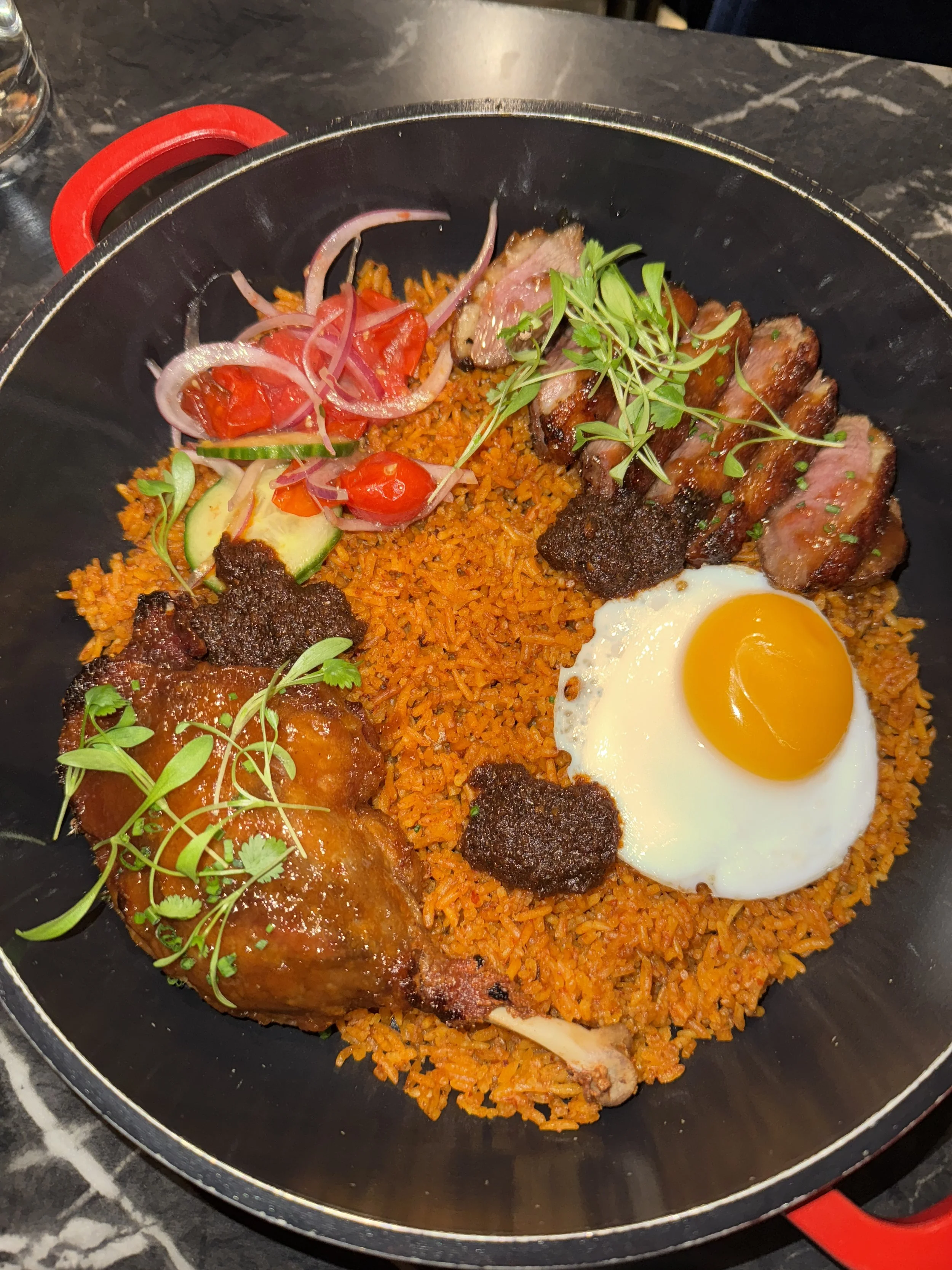 Chicken and beef with rice, a fried egg, and fresh vegetables on a black plate.