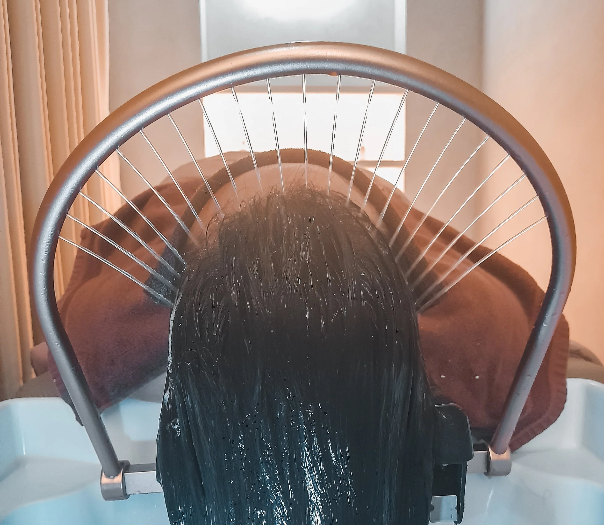 Person lying face down with wet black hair in a hair washing basin at a salon or spa.