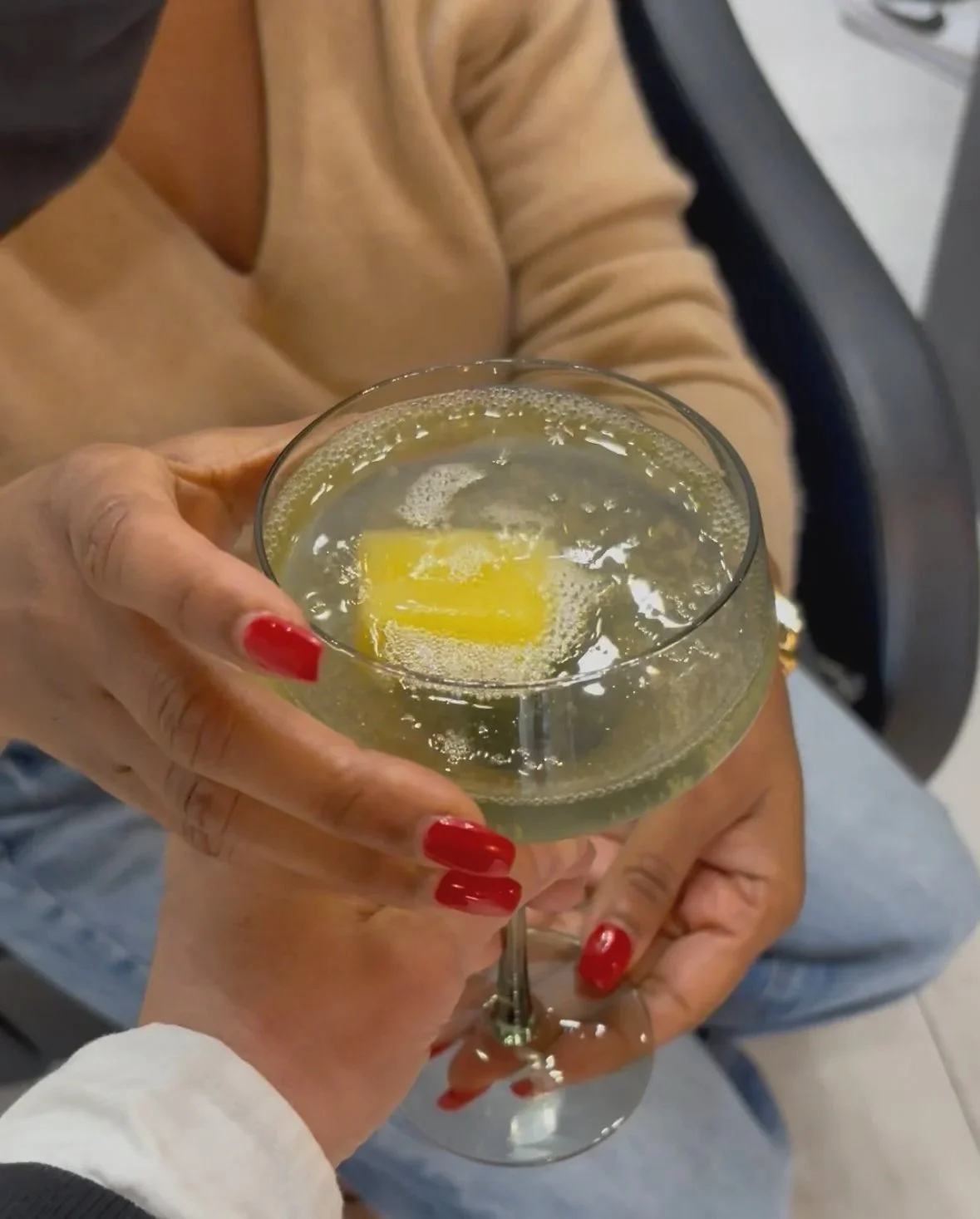 Two women holding a glass of champagne with a lemon wedge inside, celebrating indoors.