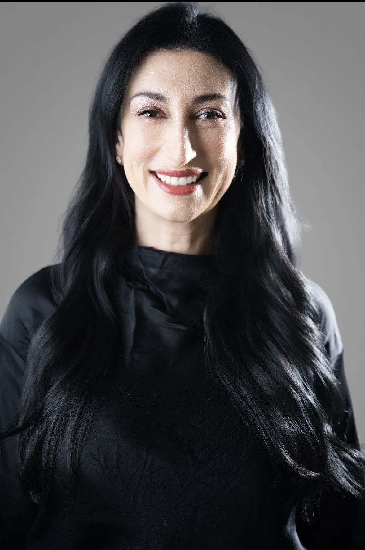 Woman taking a mirror selfie, wearing a black long-sleeve top and black leather pants in a fitting room.