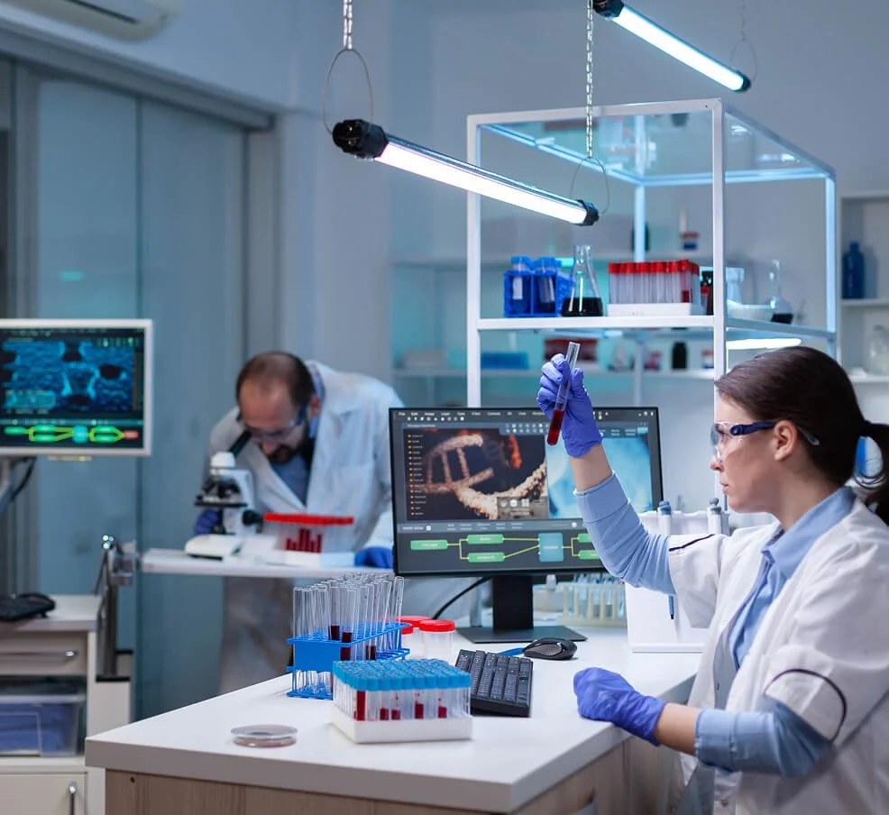 Scientists working in a modern laboratory with test tubes, a microscope, and computer monitors displaying scientific data.