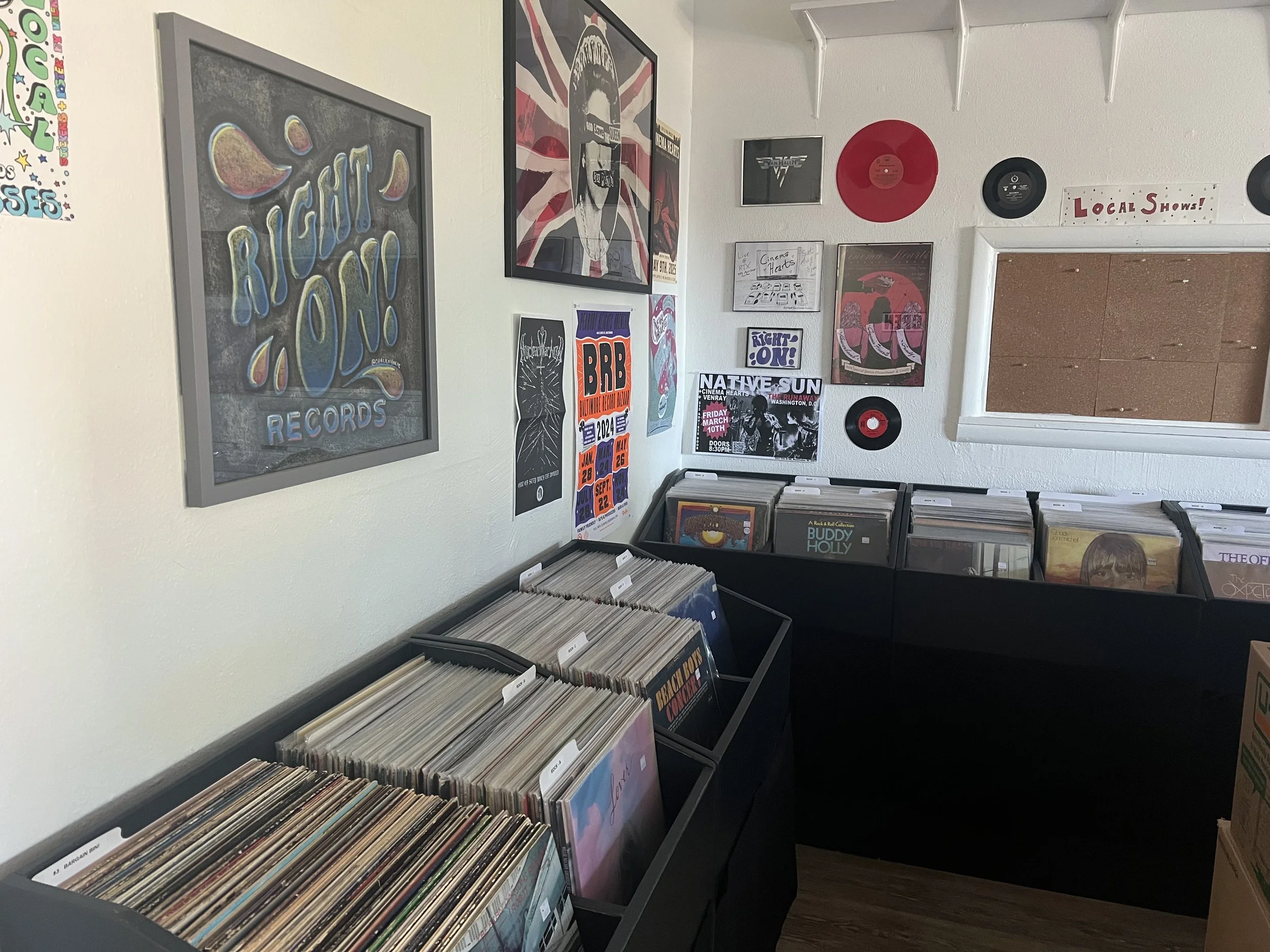 A wall decorated with music and event posters in a record store with vinyl records in bins.