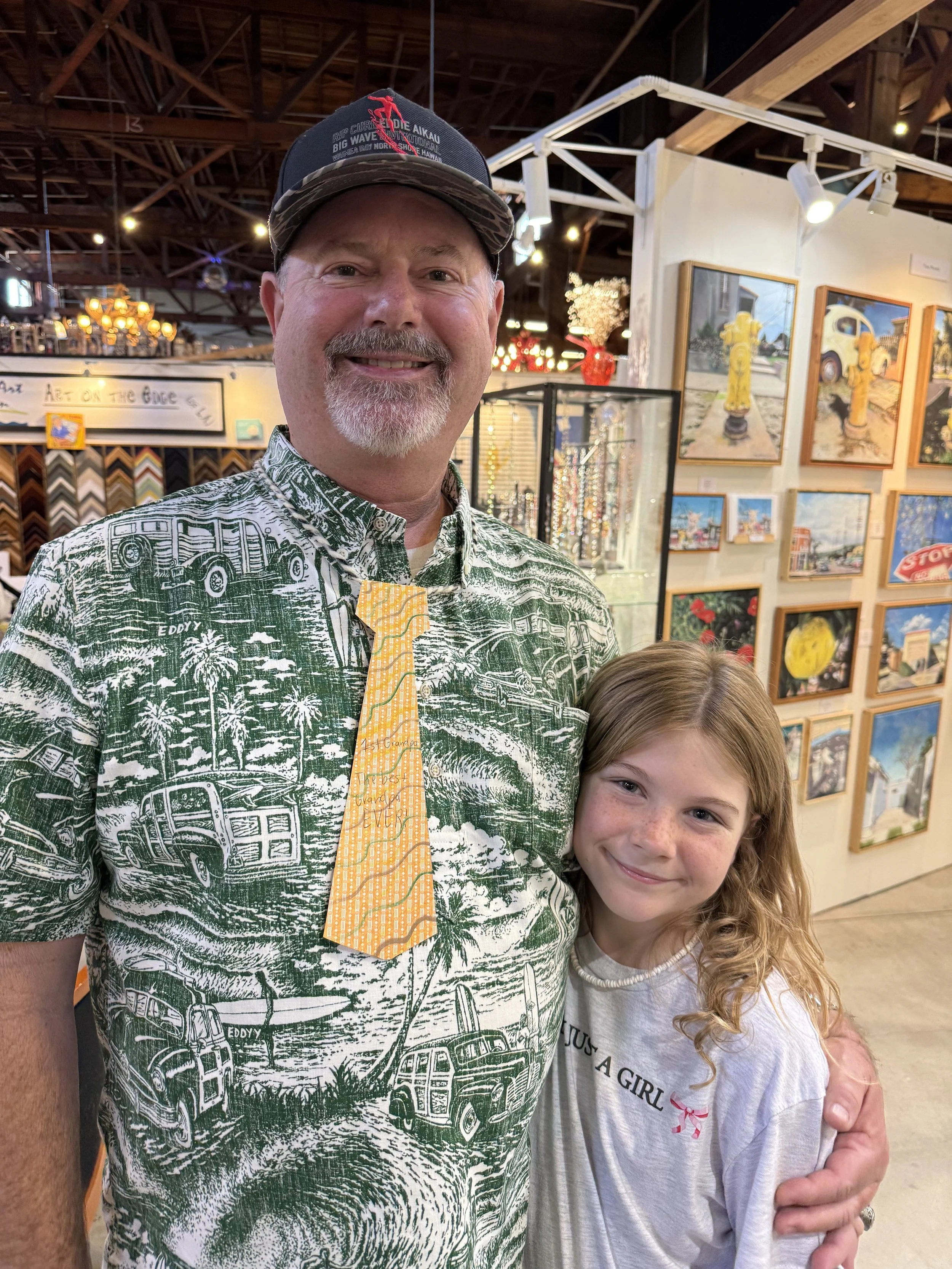 A man and a young girl smiling and posing for a photo at an art gallery or museum, with artwork displayed on walls in the background.