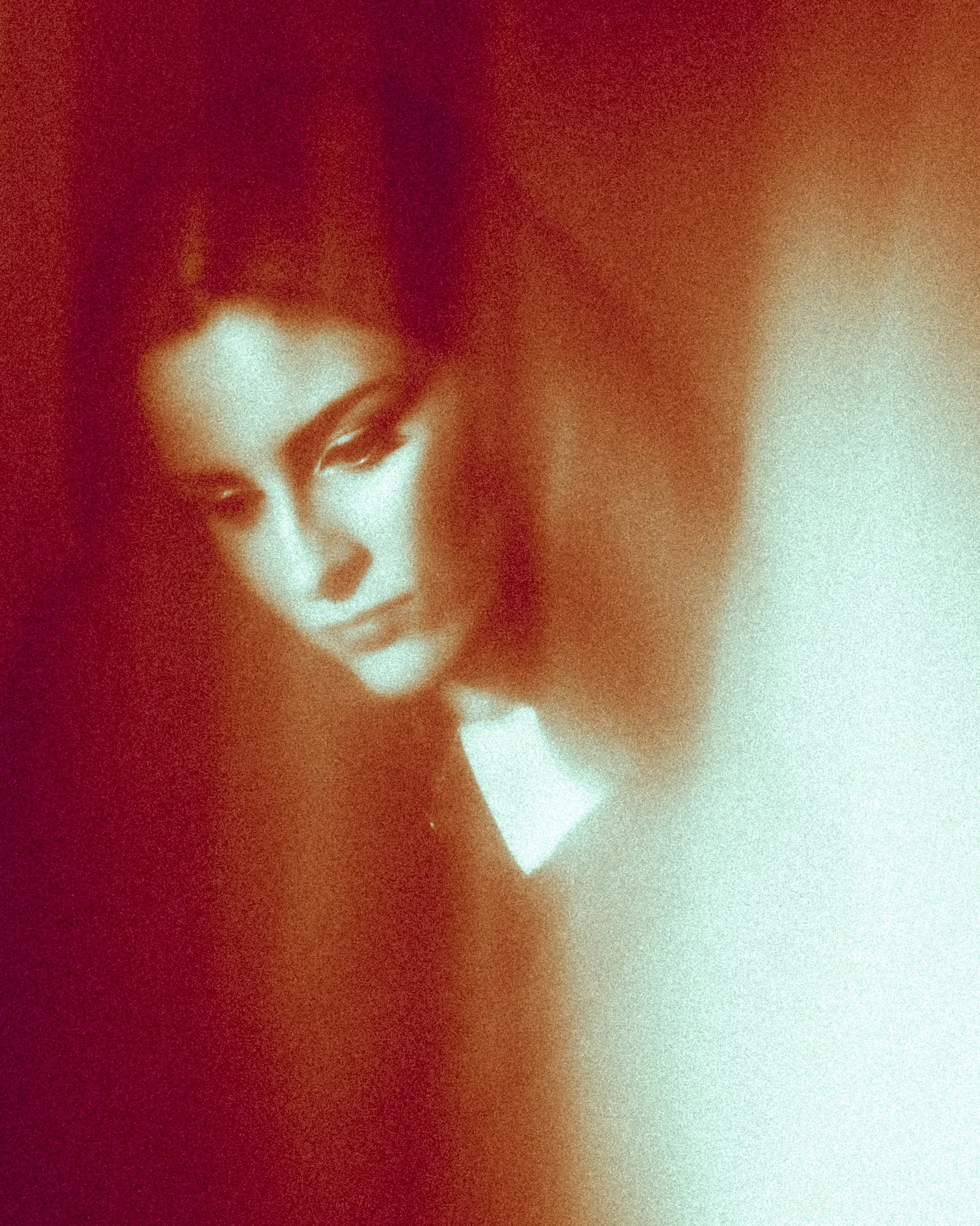 A close-up of a person's face with red hair, white skin, and minimal makeup, partially obscured by a gradient overlay in red, orange, and cream tones.
