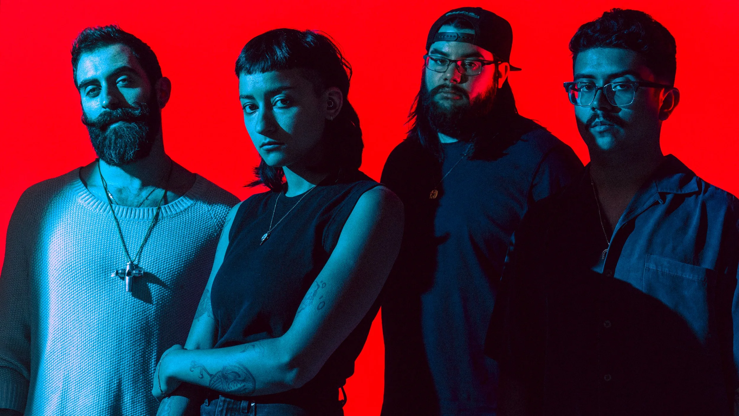 Four diverse individuals standing against a red background, illuminated with blue lighting, looking at the camera best for music promotion or tour poster or eye catching social media post