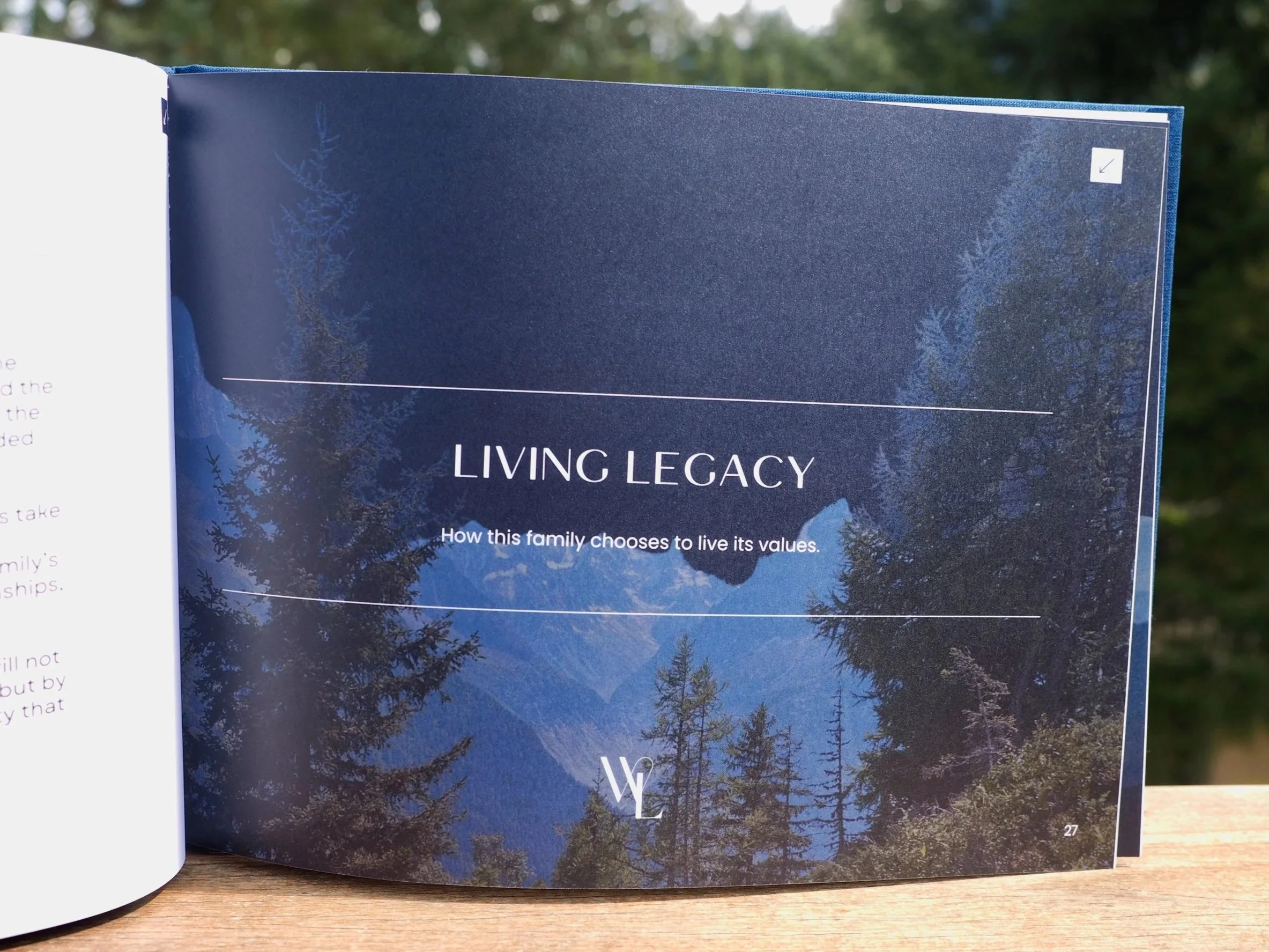 Open book titled "Living Legacy" with background image of trees and blue sky, resting on a wooden surface outdoors.