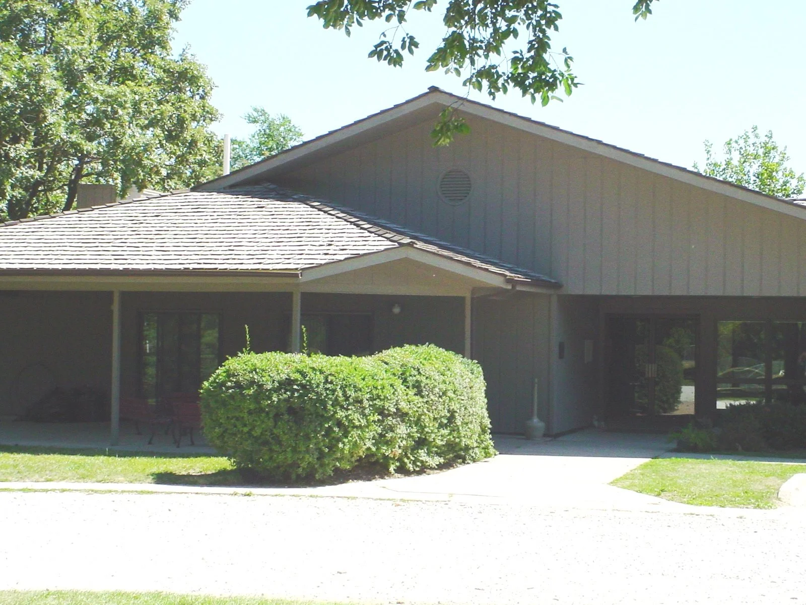 A single-story building with a peaked roof, surrounded by green bushes and trees.