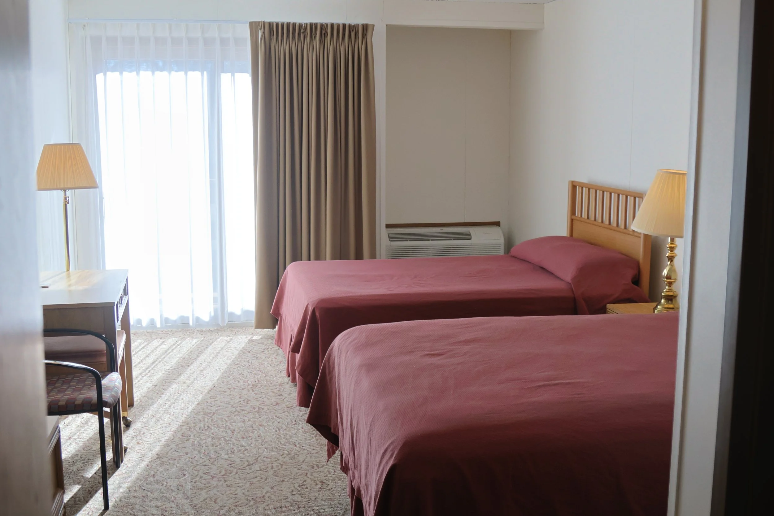 Room with two queen beds, bedside lamps, a window with curtains, and an air conditioning unit.