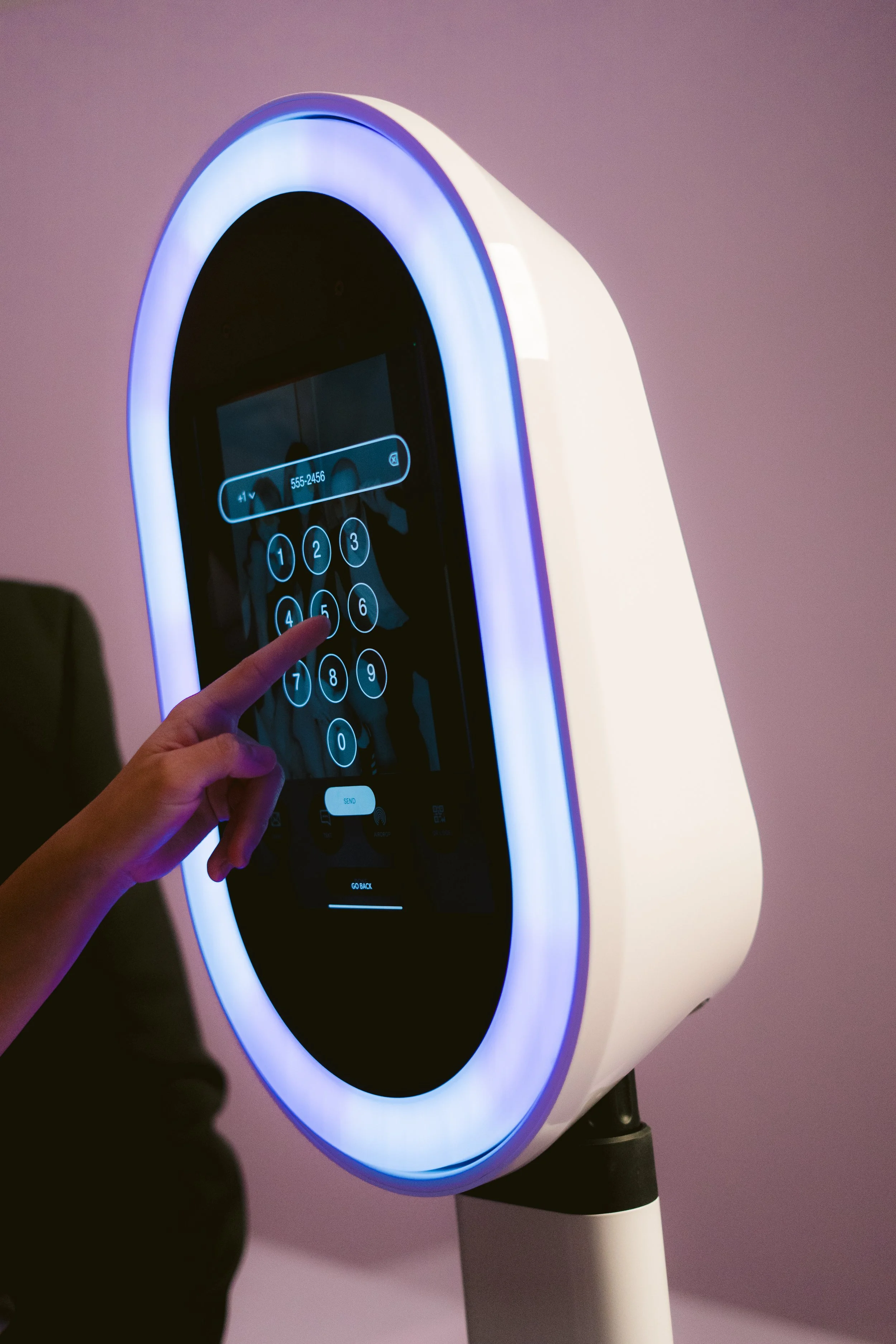 A person using a touchscreen kiosk with a circular, glowing frame in a pink-lit environment.