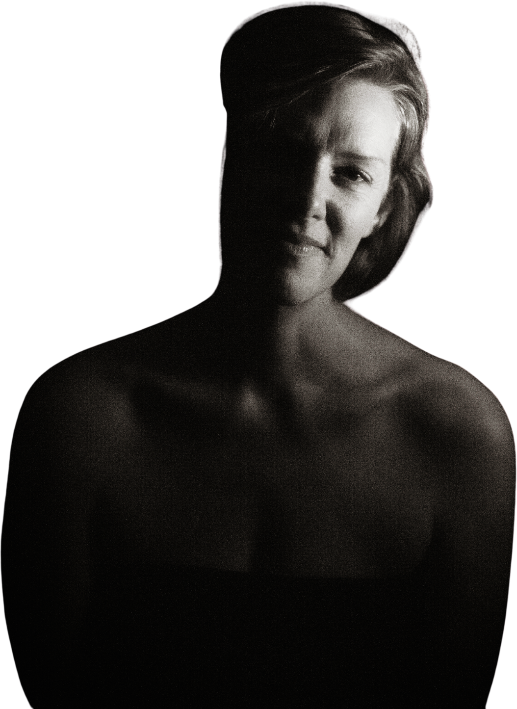 Black and white portrait of a woman with short hair, smiling, with shadows across her face and bare shoulders, against a dark background.
