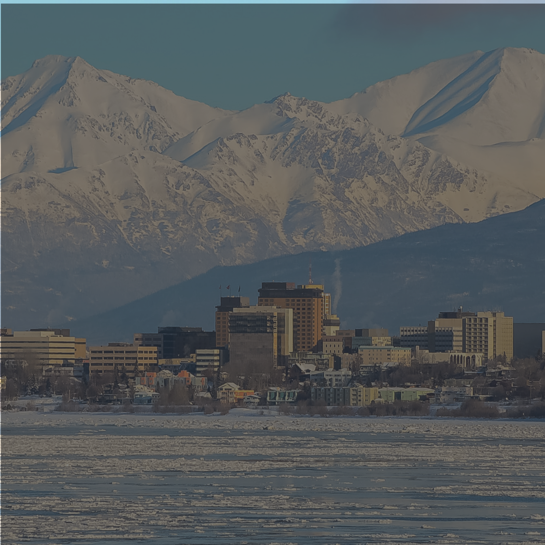 Cityscape with buildings in front of snow-covered mountains under a clear sky